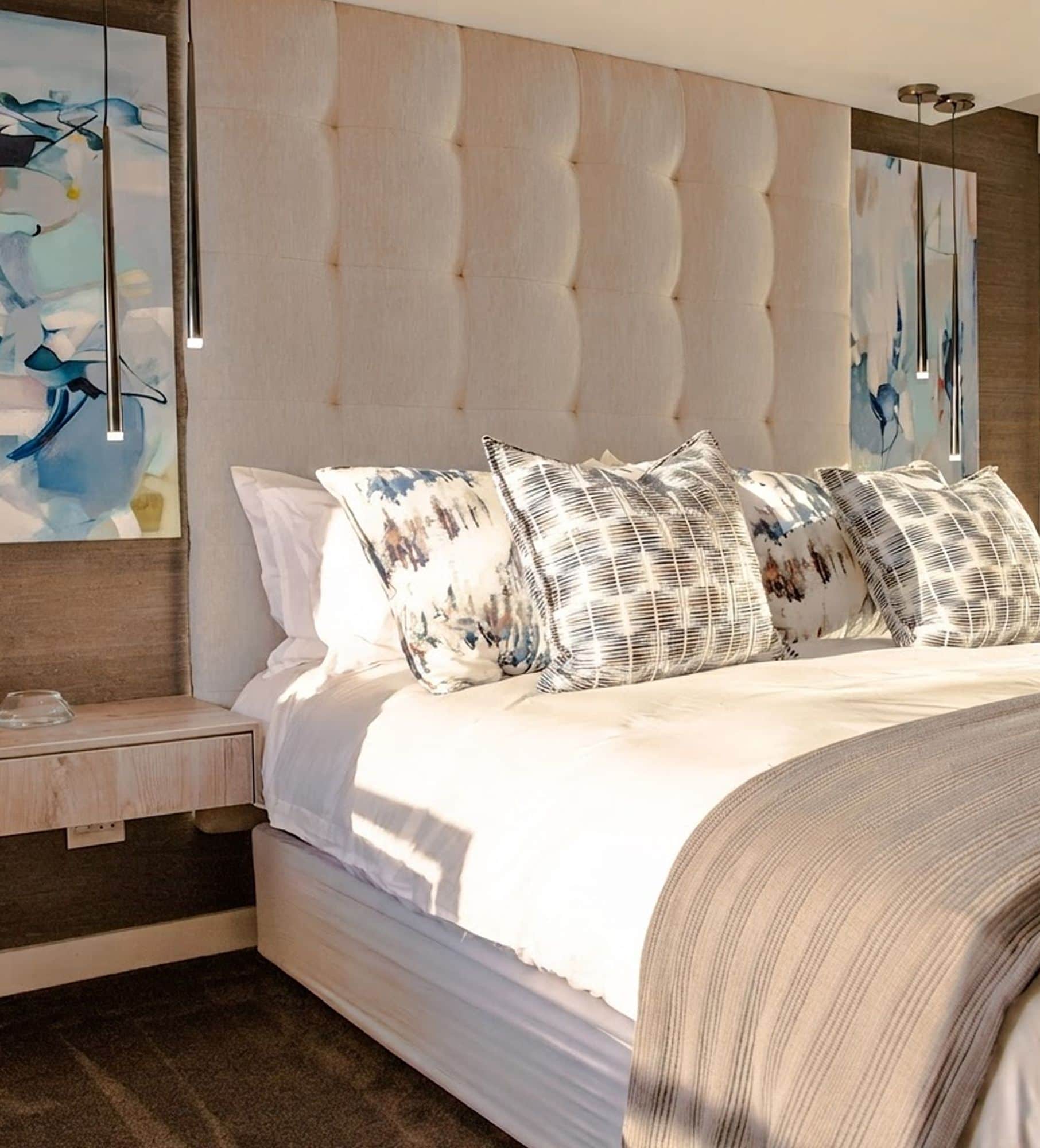 Bed with a tall tufted headboard, patterned cushions and abstract artwork on either side