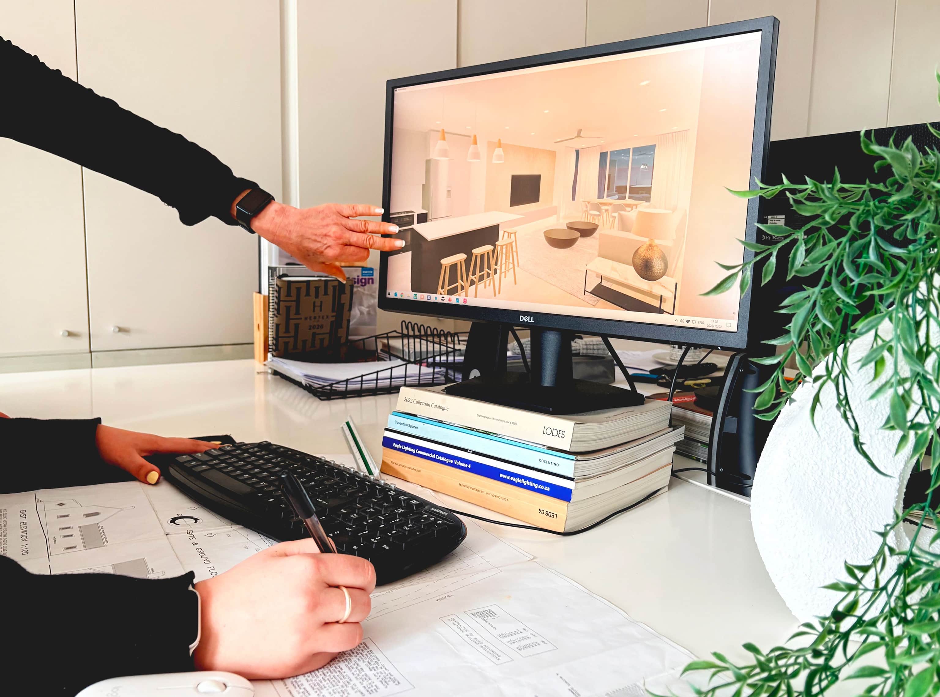 Designer presenting a 3D kitchen rendering on a computer screen while a colleague takes notes
