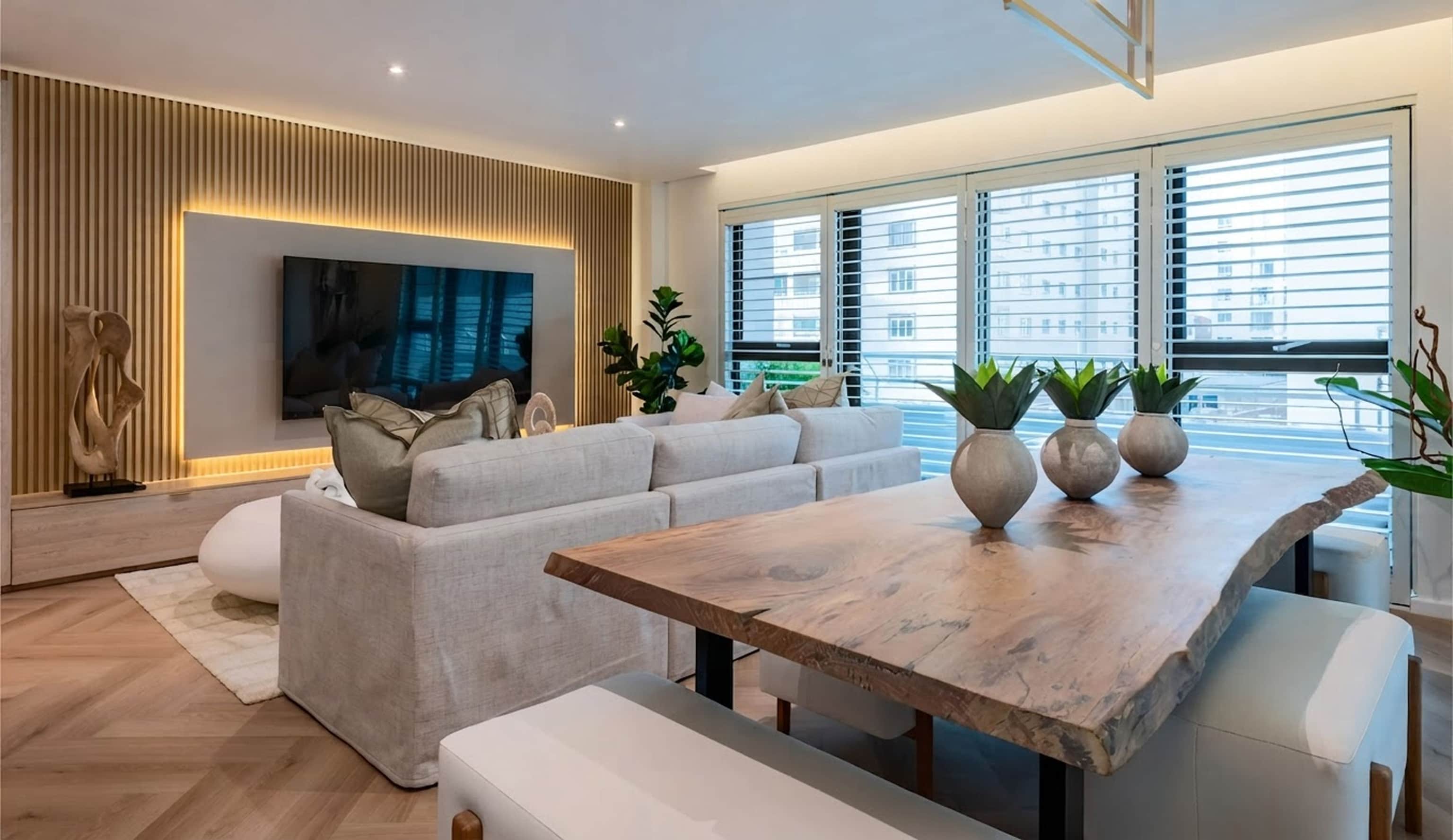 Live-edge wooden dining table with succulent vases beside a sofa and a slatted oak TV wall
