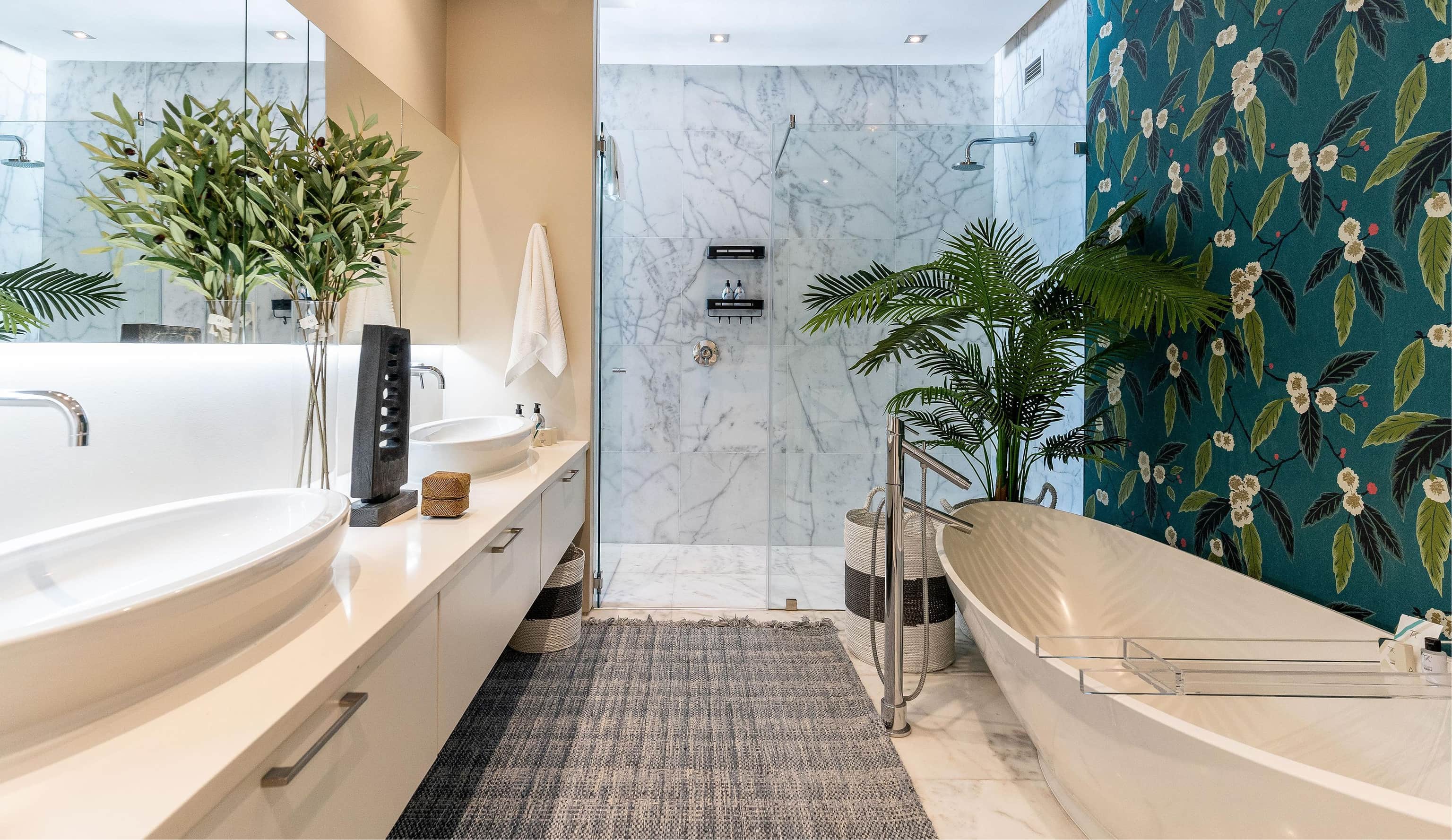 Bathroom with a freestanding bath, a marble shower, a palm and botanical wallpaper