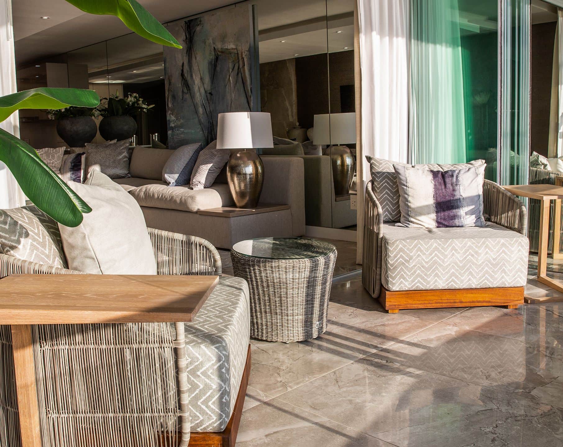 Terrace with woven armchairs and a round wicker side table on marble flooring beside folding glass doors