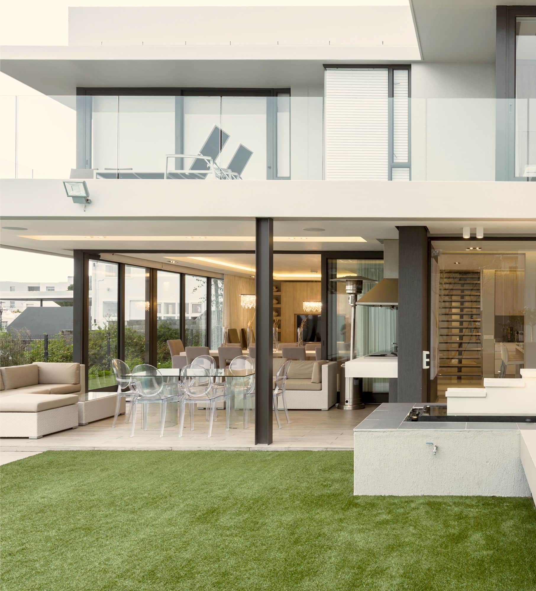 Covered patio and lawn of a modern home, with glass doors opening to the dining and lounge areas