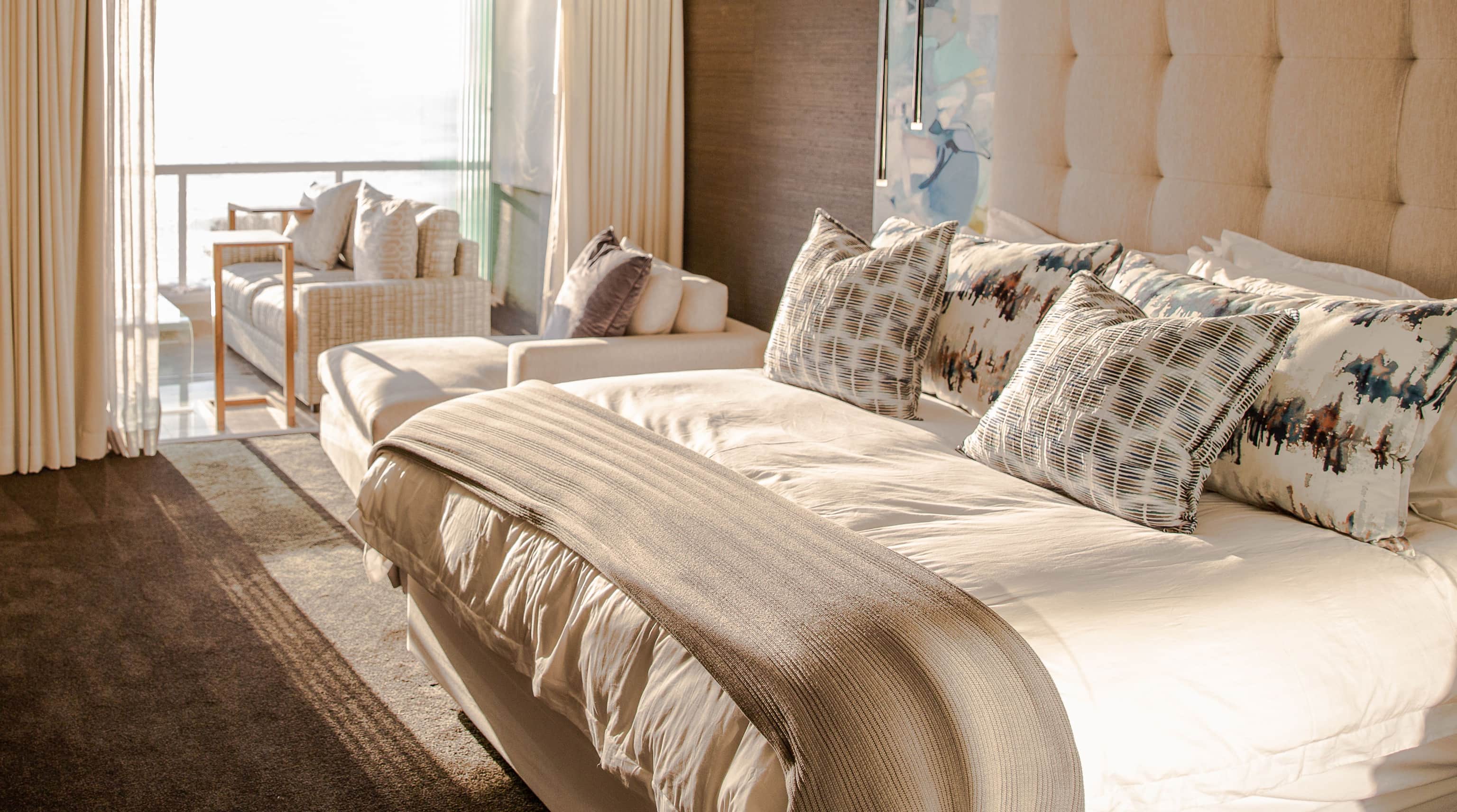 Main bedroom with a tall tufted headboard and patterned cushions, opening to a sea-facing balcony