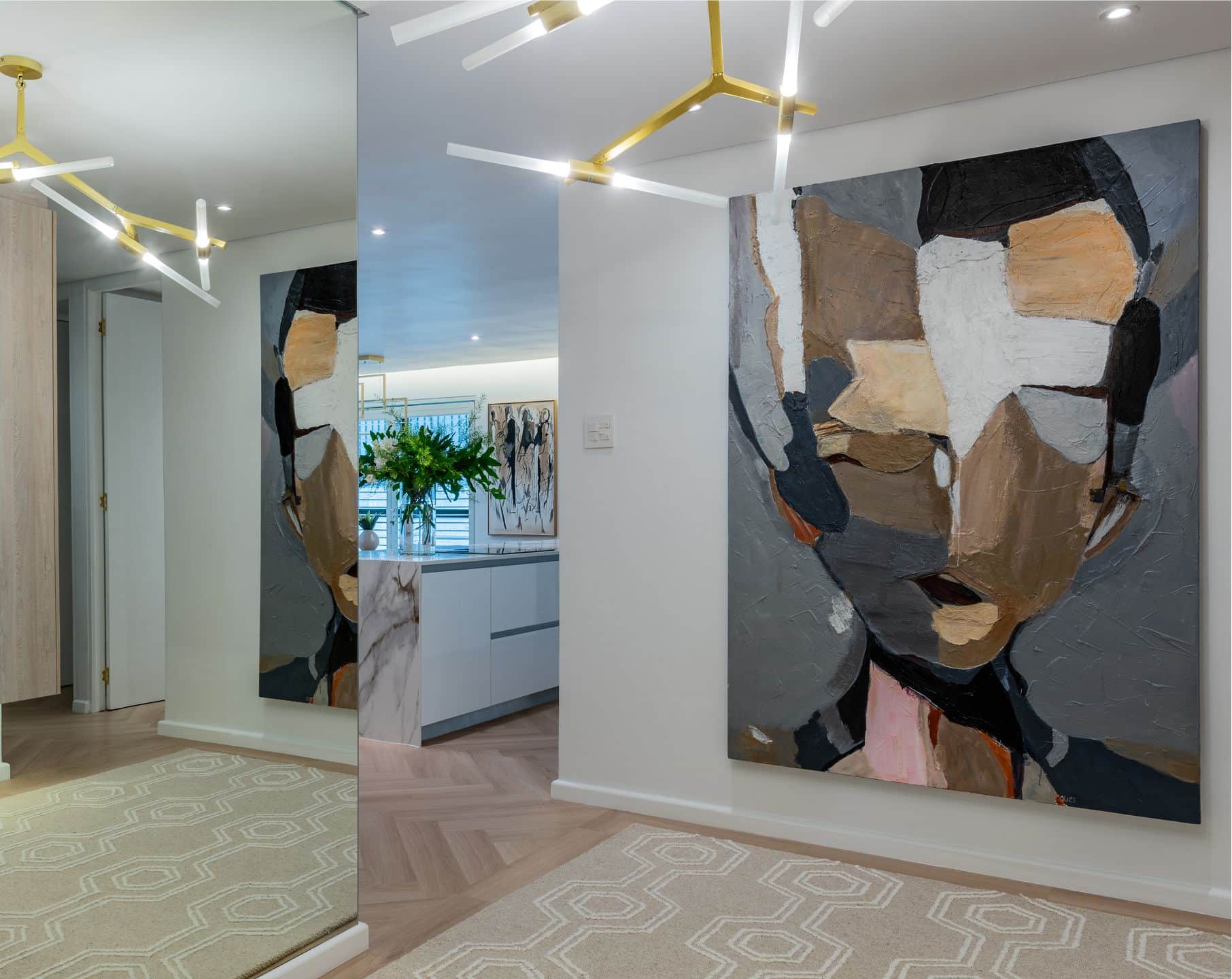 Entrance hall with a large abstract portrait painting, a brass pendant light and a mirrored wall