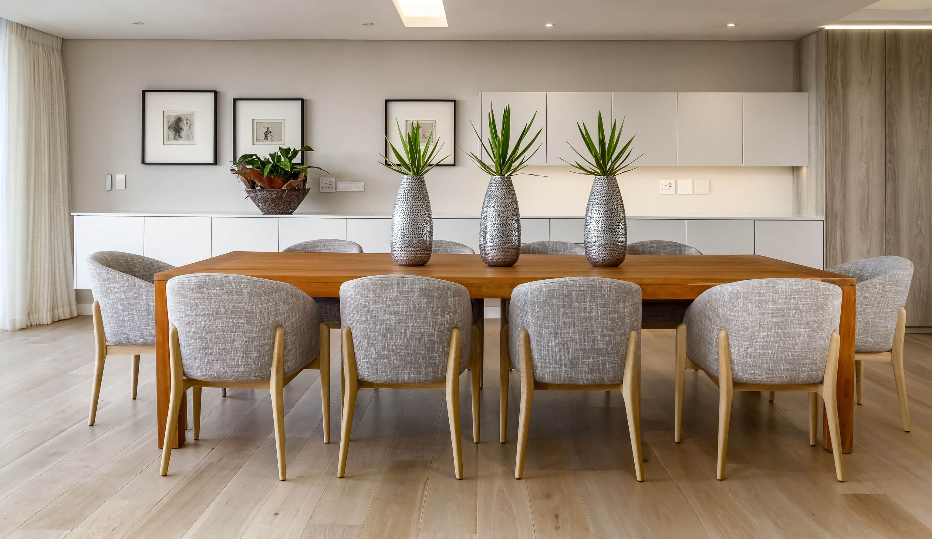 Oak dining table with grey upholstered chairs and three hammered silver vases with succulents