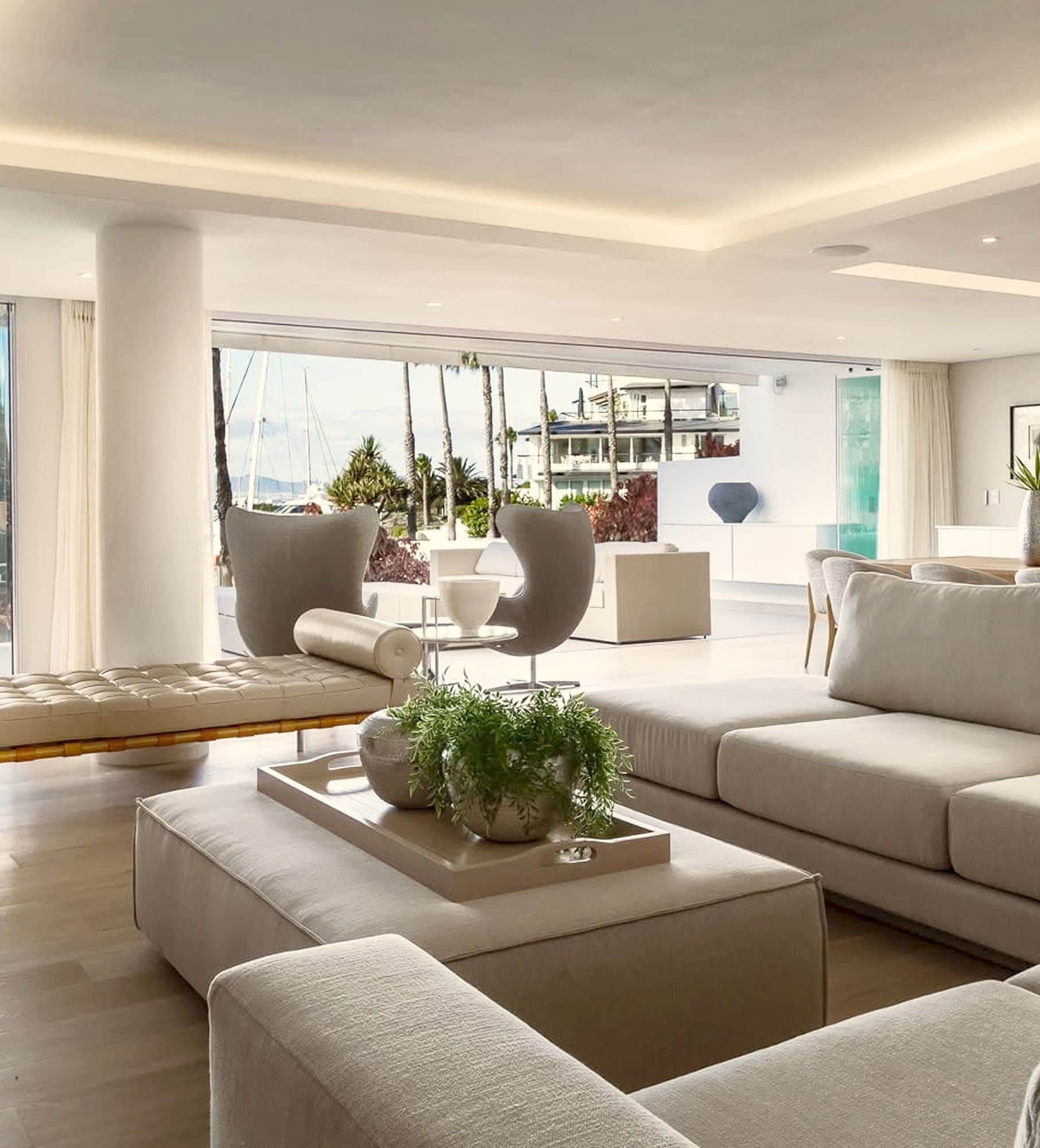 Open-plan lounge with a sectional sofa, egg chairs and a tufted daybed, open to the marina